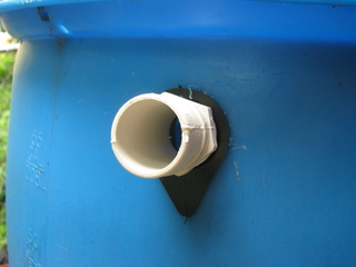 Photo of the white plastic hose adapter and black rubber
         barrel seal installed in the barrel, with the blue rain
         barrel filling most of the rest of the frame. One segment of
         the adapter is hexagonal.