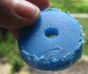 Photo of a circular chunk of blue plastic being held up
         in the foreground, about 35 mm across and 6 mm thick. In the
         background is the rain barrel.